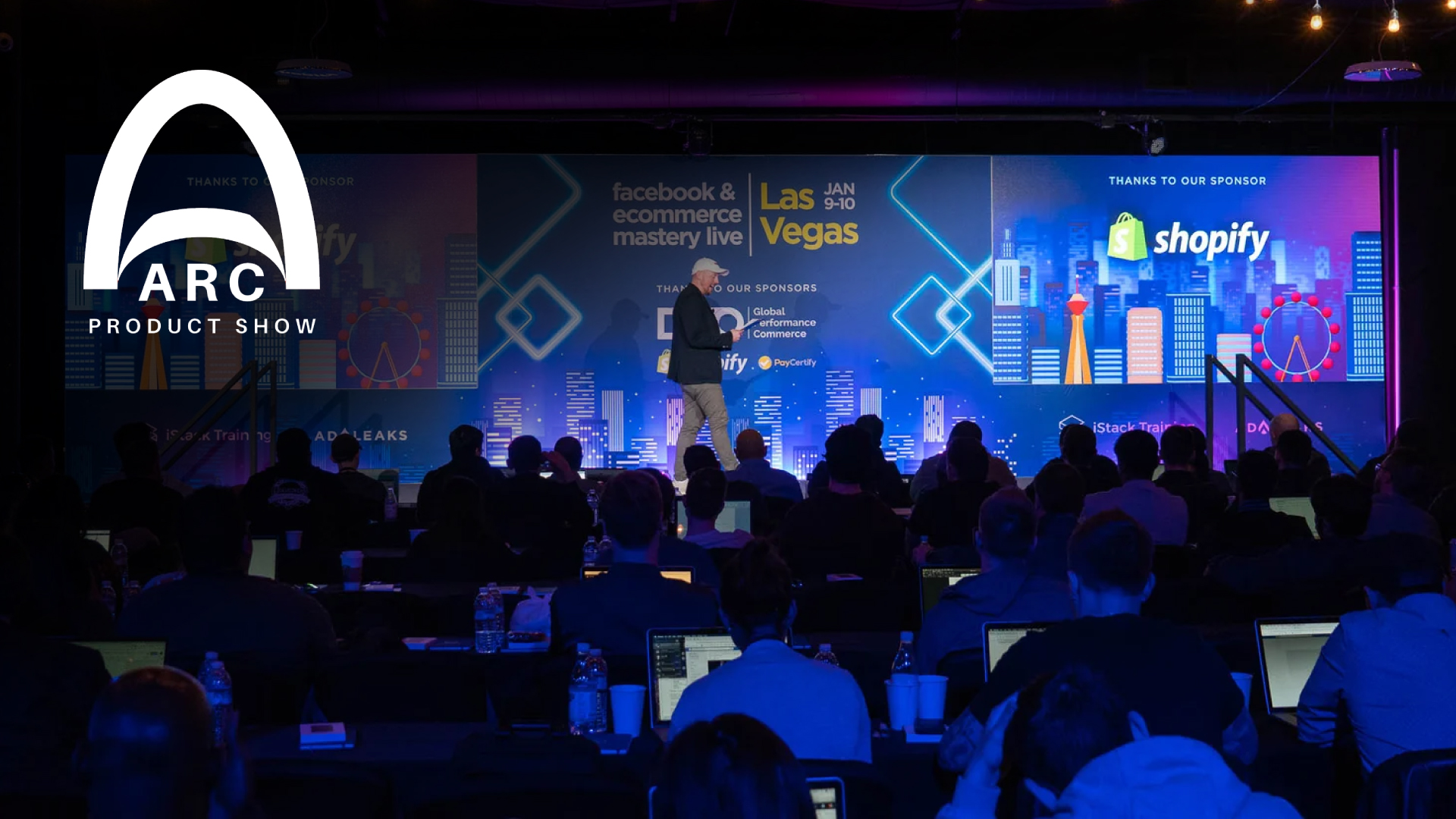 Stage at ARC Product Show with a speaker on stage and a large ARC logo on the left; illuminated blue/purple backdrop and an audience in front.